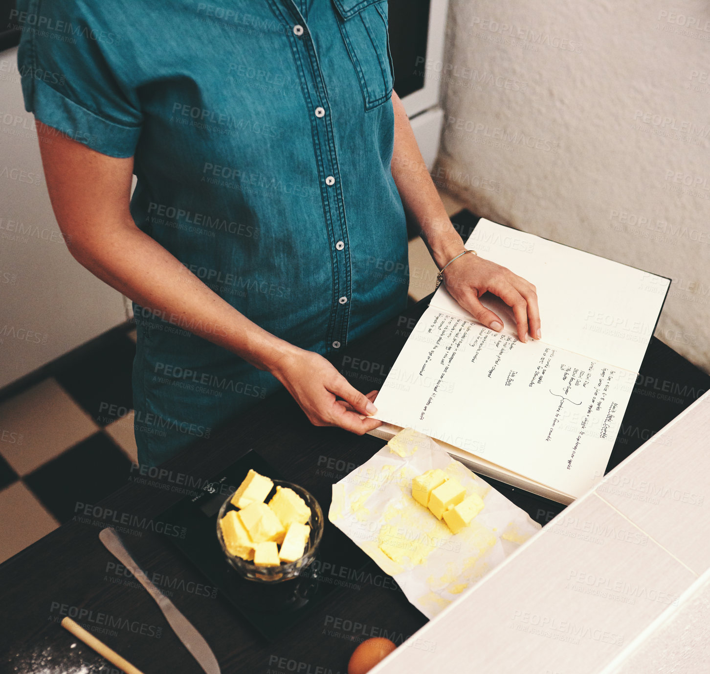 Buy stock photo Cropped shot of an unrecognizable woman reading a recipe from a book while baking at home