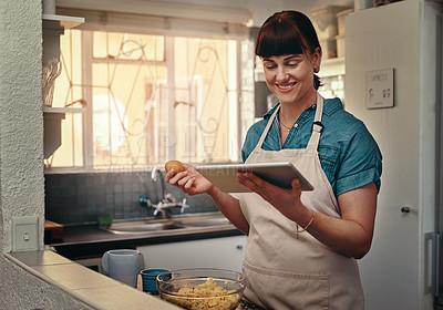 Buy stock photo Shot of an attractive young woman following an online recipe on her digital tablet while cooking inside her kitchen
