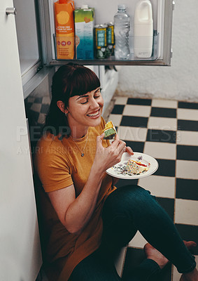 Buy stock photo Shot of an attractive young woman sitting on the floor and eating cake inside her kitchen at home