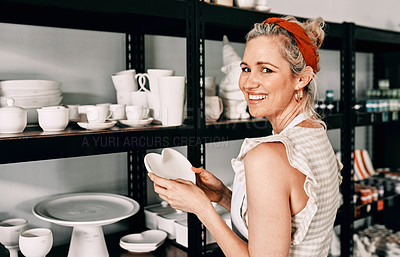 Buy stock photo Cropped portrait of an attractive mature woman standing and organising her pottery on a shelf in her workshop