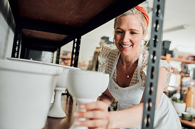 Buy stock photo Cropped shot of an attractive mature woman standing and organising her pottery on a shelf in her workshop