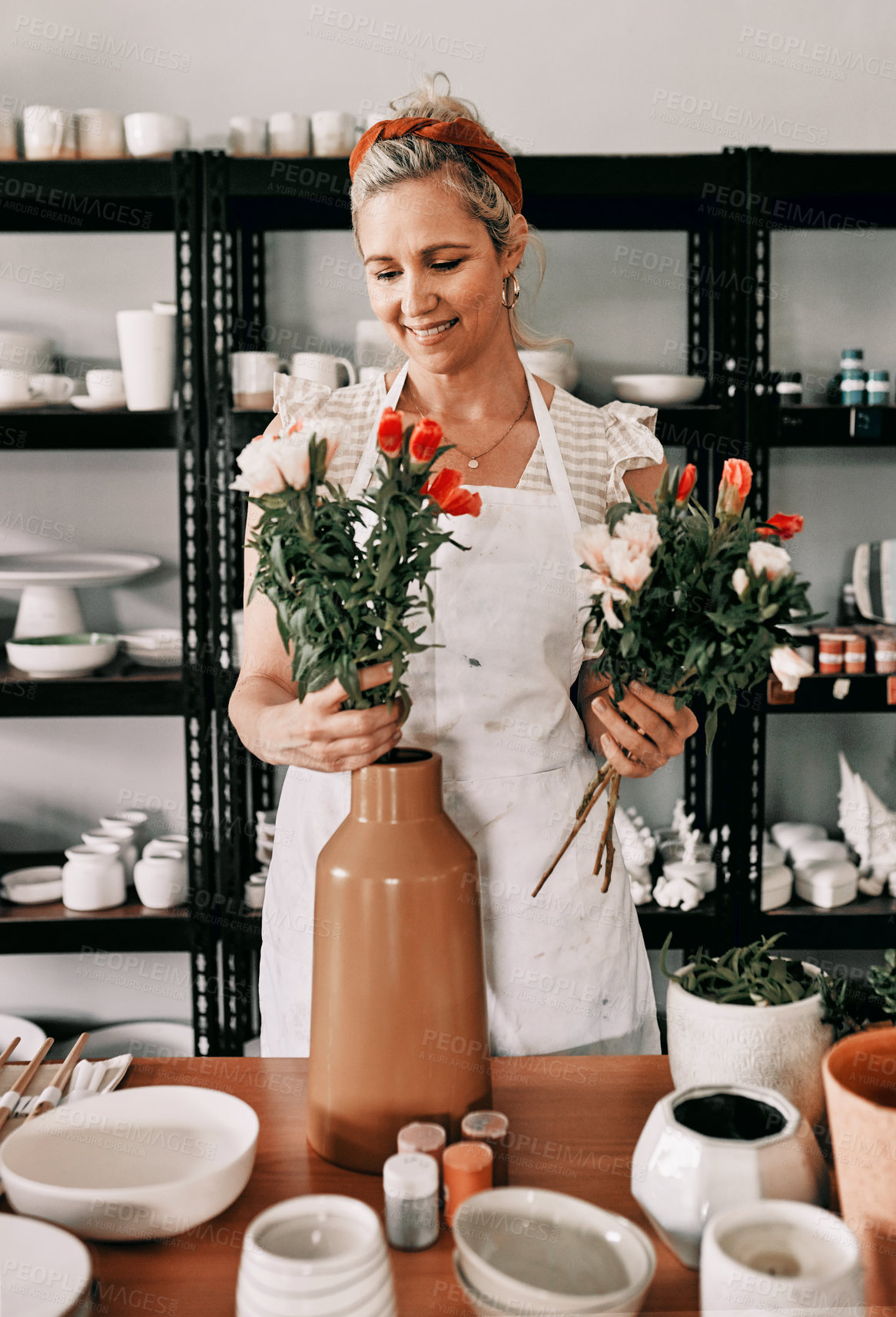 Buy stock photo Cropped shot of an attractive mature woman standing alone and putting flowers into a handmade vase in her pottery workshop