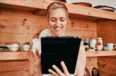 Buy stock photo Cropped shot of an attractive mature woman standing alone and using a tablet in her pottery workshop