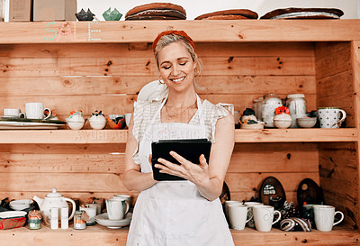 Buy stock photo Cropped shot of an attractive mature woman standing alone and using a tablet in her pottery workshop