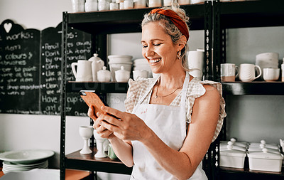 Buy stock photo Cropped shot of an attractive mature woman standing alone and using her cellphone in her pottery workshop