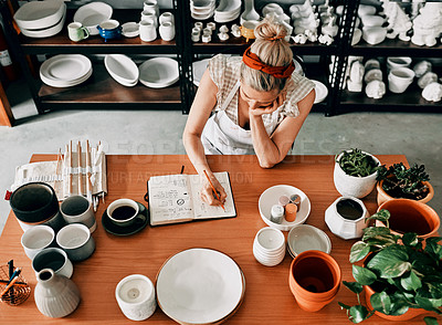 Buy stock photo High angle shot of an unrecognizable woman sitting and sketching in a notebook in her pottery workshop