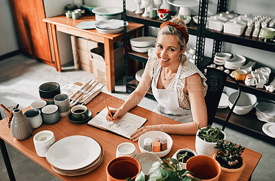 Buy stock photo High angle portrait of an attractive mature woman sitting alone in her pottery workshop and sketching in a notebook