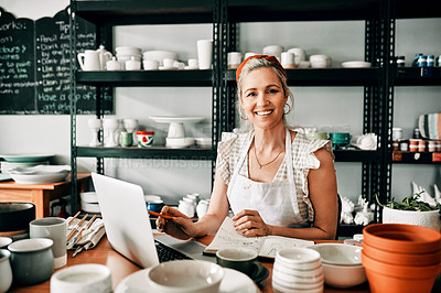 Buy stock photo Cropped portrait of an attractive mature woman sitting alone and using her laptop in her pottery workshop