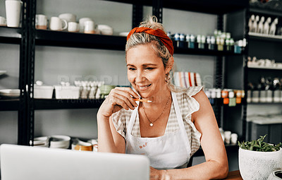 Buy stock photo Cropped shot of an attractive mature woman sitting alone and using her laptop in her pottery workshop
