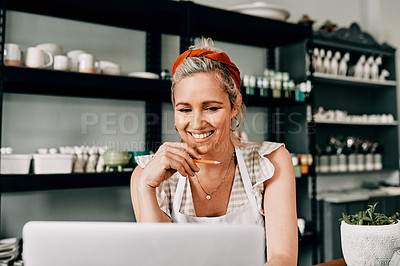 Buy stock photo Cropped shot of an attractive mature woman sitting alone and using her laptop in her pottery workshop