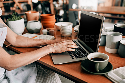 Buy stock photo Cropped shot of an unrecognizable woman sitting and using her laptop in her pottery workshop