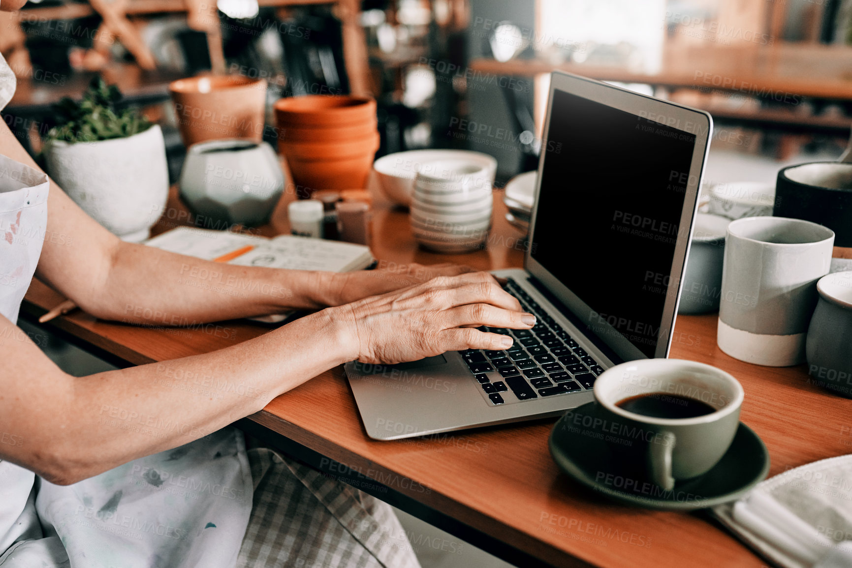 Buy stock photo Cropped shot of an unrecognizable woman sitting and using her laptop in her pottery workshop