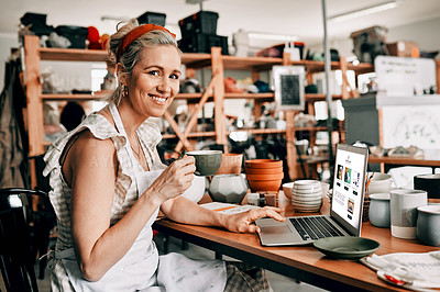 Buy stock photo Cropped portrait of an attractive mature woman sitting alone and using her laptop in her pottery workshop while drinking coffee