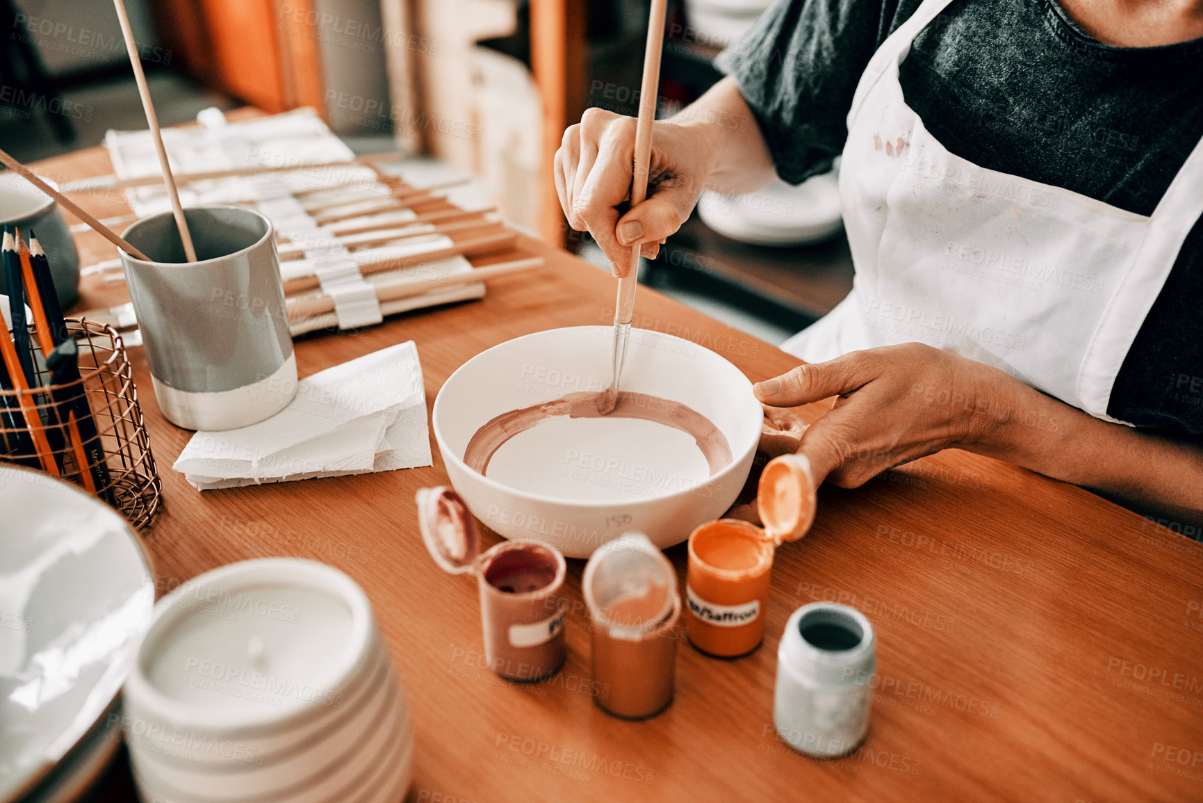 Buy stock photo Cropped shot of an unrecognizable woman sitting alone and painting a pottery bowl in her workshop