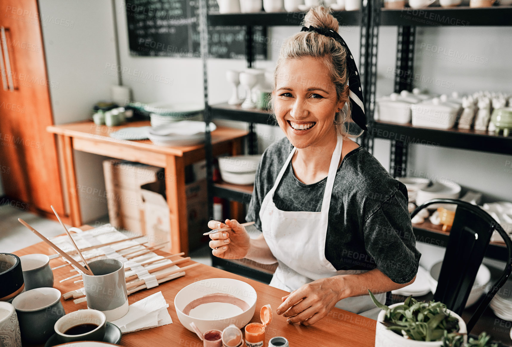 Buy stock photo Cropped portrait of an attractive mature woman sitting alone and painting a pottery bowl in her studio