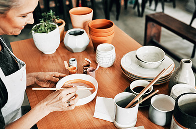Buy stock photo Cropped shot of an attractive mature woman sitting alone and painting a pottery bowl in her studio