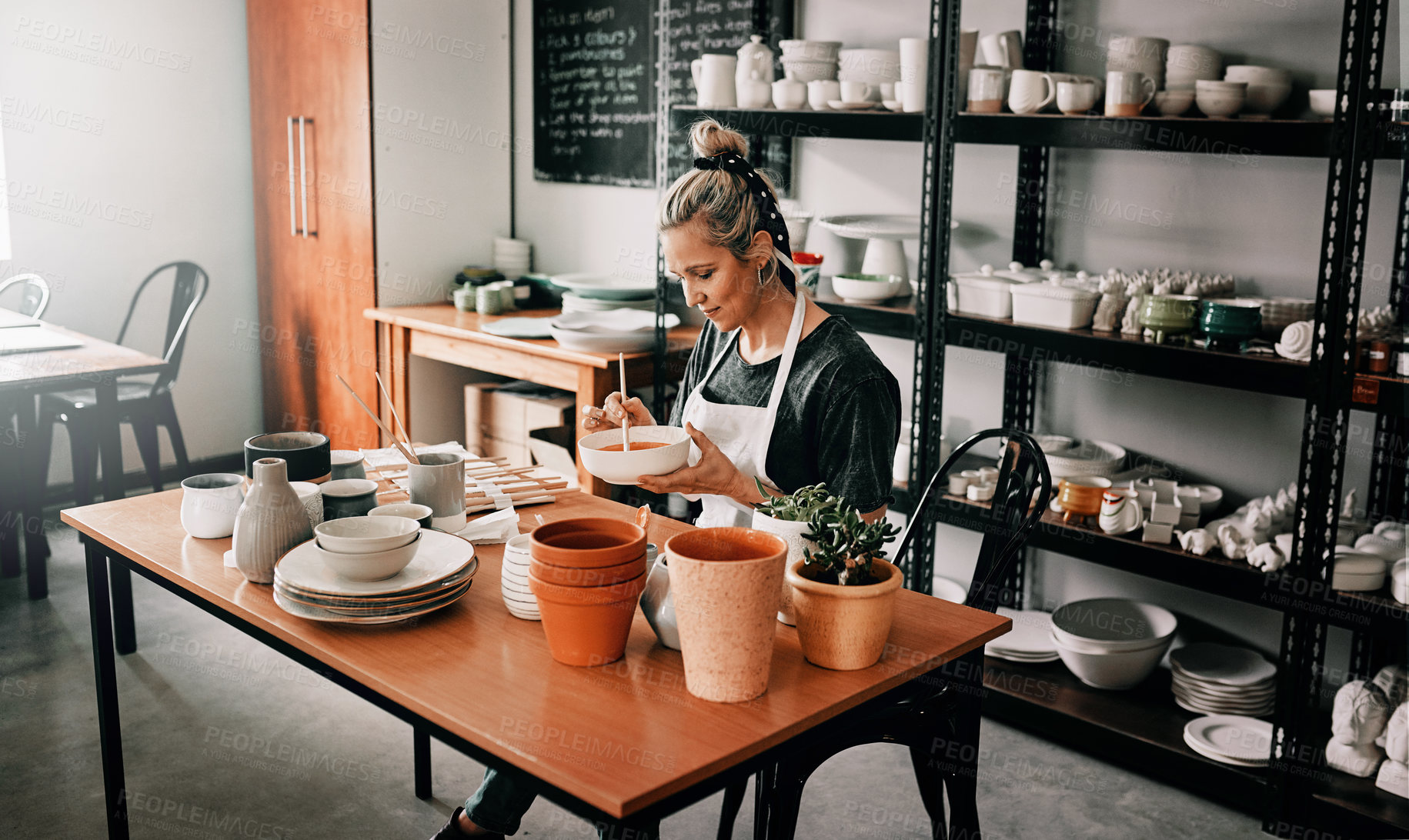 Buy stock photo Cropped shot of an attractive mature woman sitting alone and painting a pottery bowl in her studio