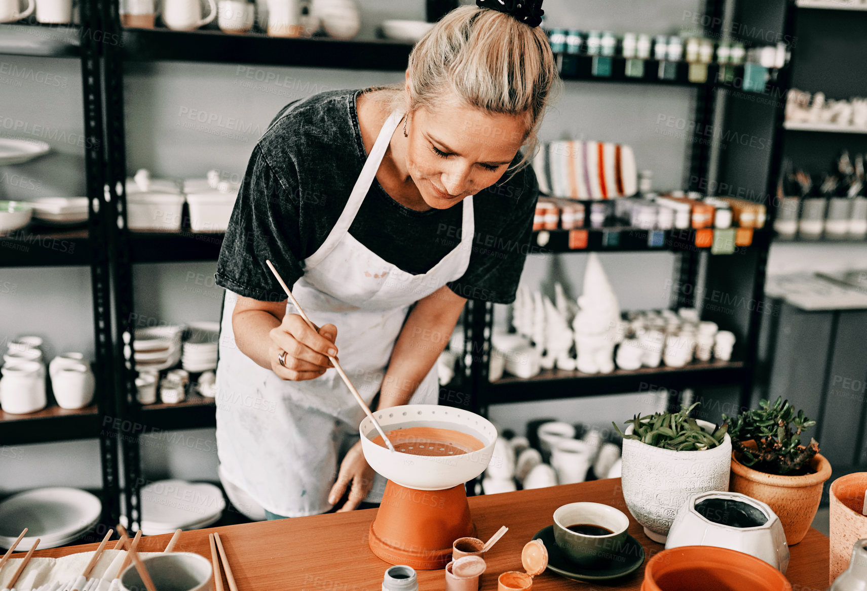 Buy stock photo Cropped shot of an attractive mature woman standing alone and painting a pottery bowl in her workshop