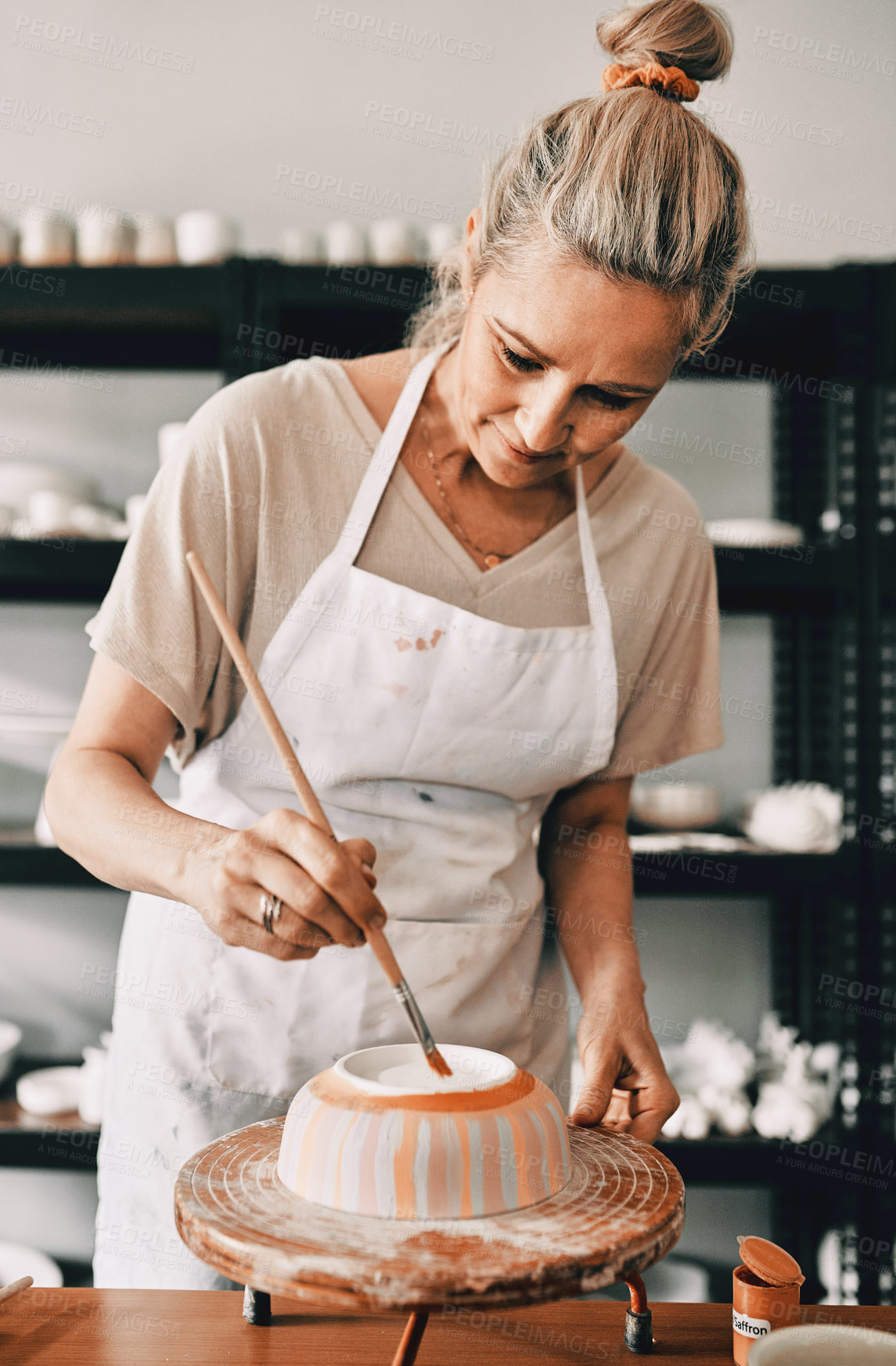 Buy stock photo Cropped shot of an attractive mature woman standing alone and painting a pottery bowl in her studio
