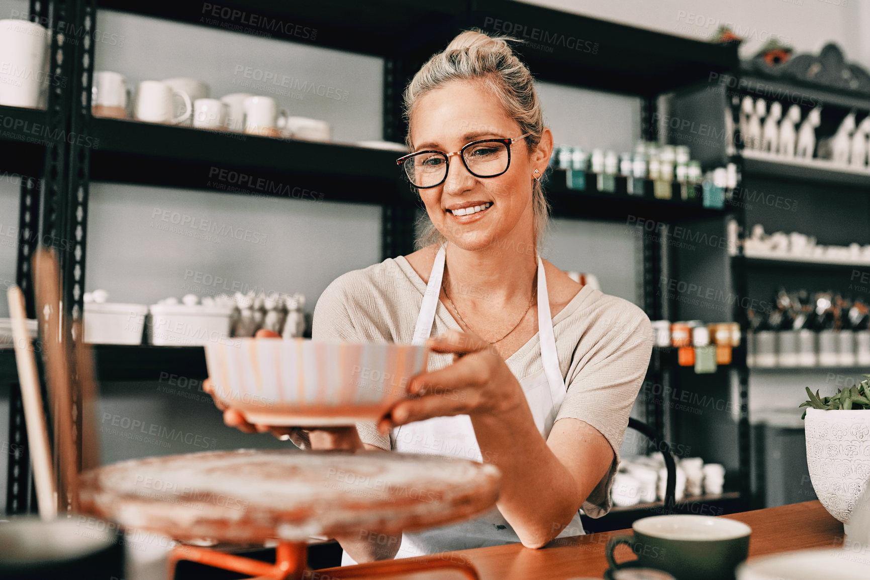 Buy stock photo Cropped shot of an attractive mature woman sitting alone and admiring her finished pottery in her workshop