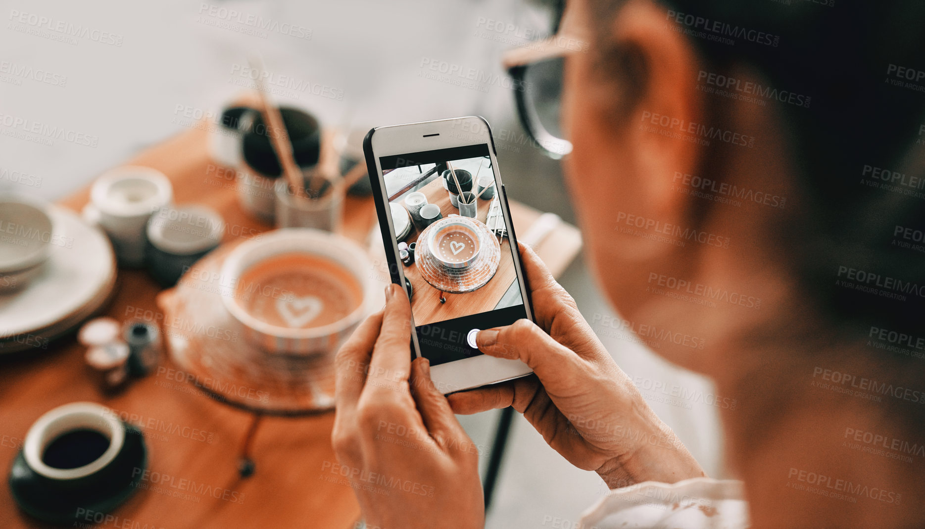 Buy stock photo Cropped shot of an unrecognizable woman standing and taking a picture of her pottery with her cellphone in her workshop