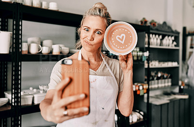 Buy stock photo Cropped shot of an attractive mature woman using her cellphone to take a selfie with her pottery in her studio