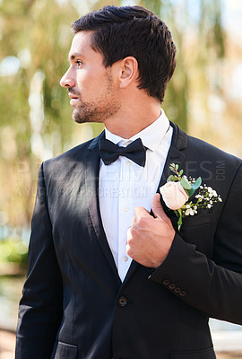 Buy stock photo Shot of a handsome young bridegroom adjusting his suit and getting ready outdoors on his wedding day