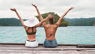 Buy stock photo Rear view, people sitting on a jetty and carefree for excitement outdoors by the ocean. Summer vacation or holiday break, freedom and excited or cheerful women sit on pier at sea for fresh air