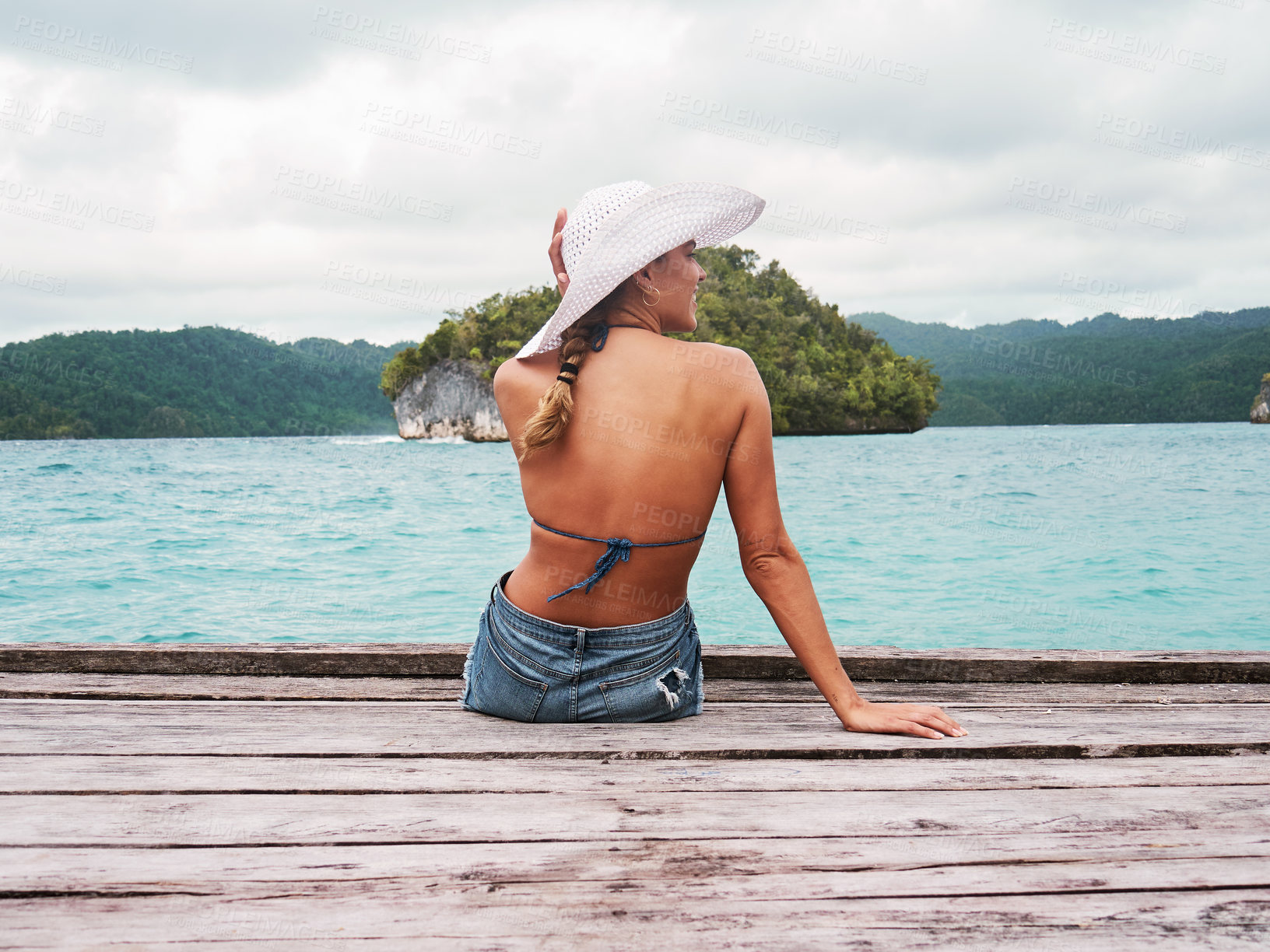 Buy stock photo Adventure, hat and woman on an island to relax while on tropical summer vacation or holiday. Travel, outdoor and back of female person sitting on wood pier by ocean water on weekend trip in paradise.