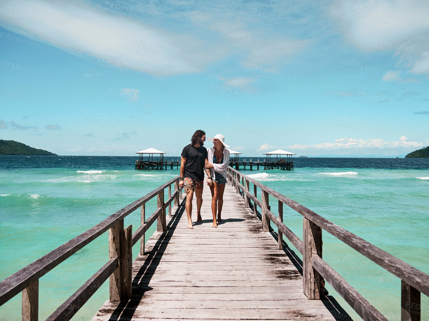 Buy stock photo Shot of a carefree young couple walking on a jetty together next to the ocean during the day