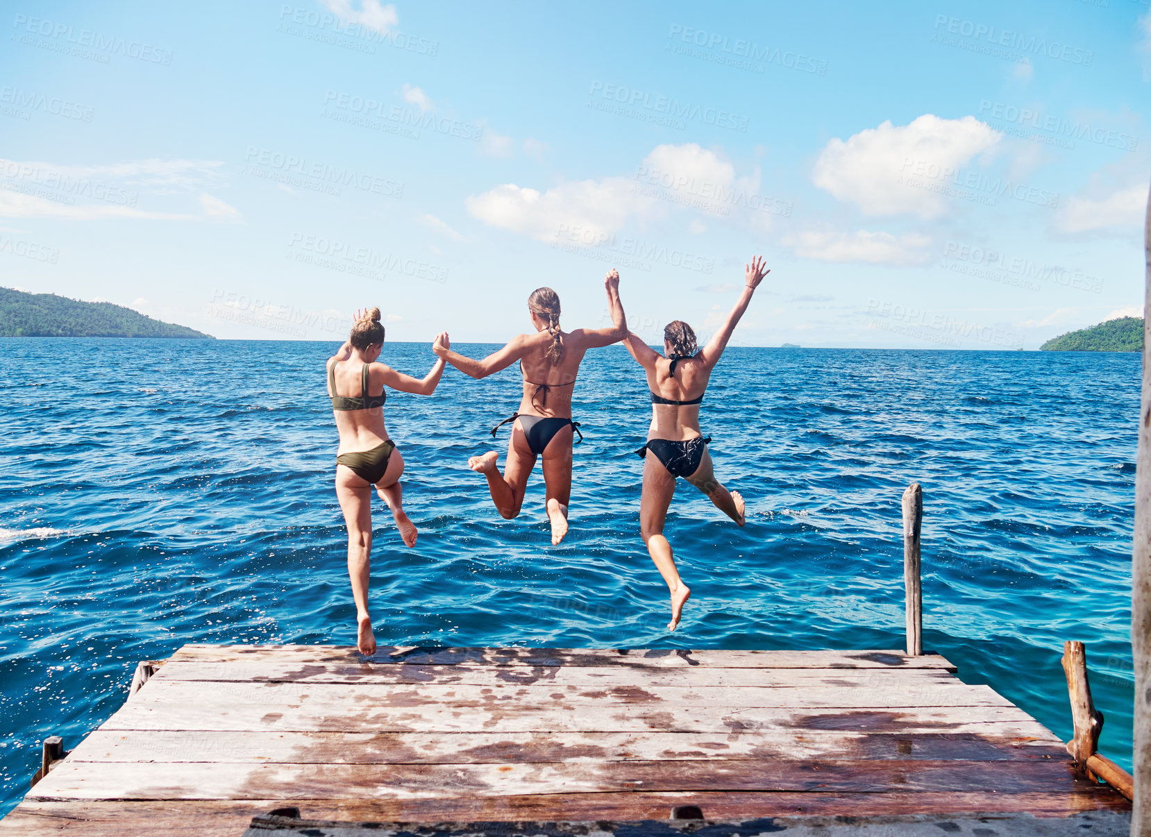 Buy stock photo Rearview shot of a group of young women jumping off a pier and into the ocean together