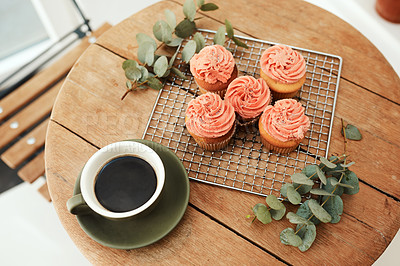 Buy stock photo High angle shot of freshly baked cupcakes on a metal tray and a cup of coffee on a table indoors