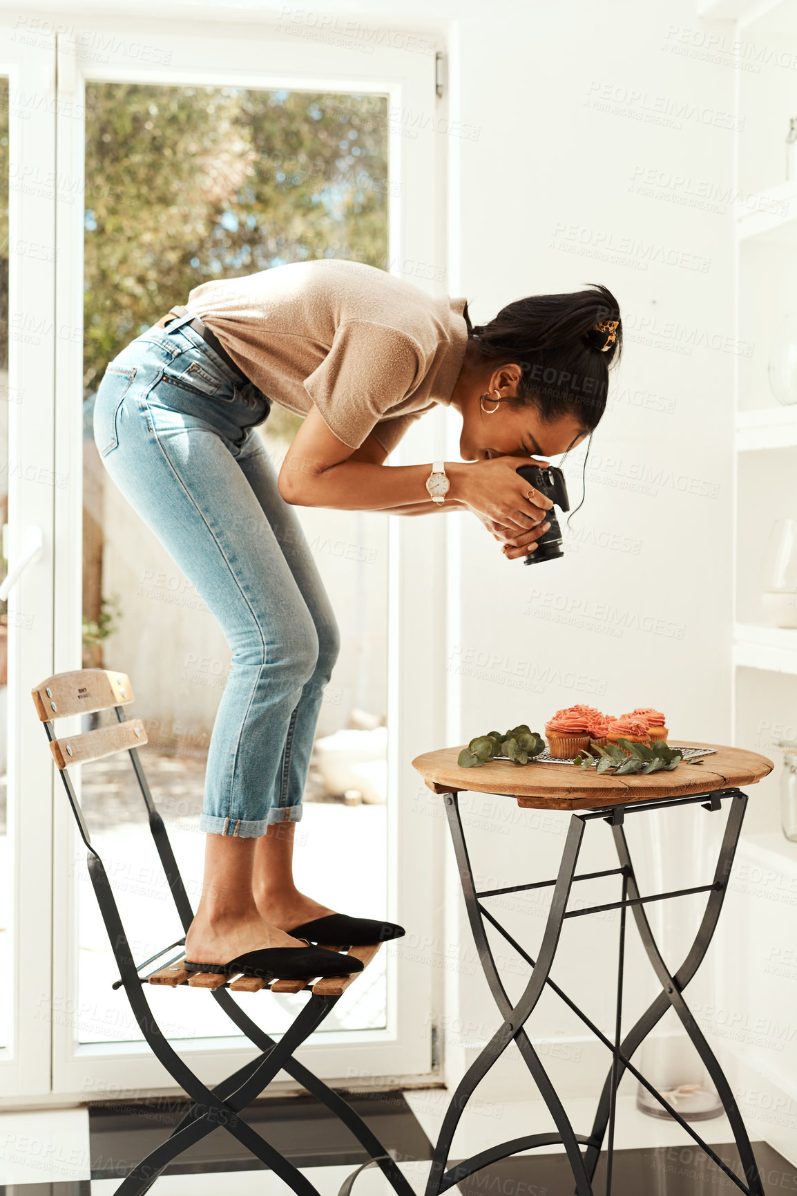 Buy stock photo Full length shot of an attractive young businesswoman standing and using her camera to photograph cupcakes for her blog