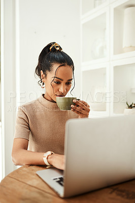 Buy stock photo Cropped shot of an attractive young businesswoman sitting and enjoying a cup of coffee while using her laptop at home