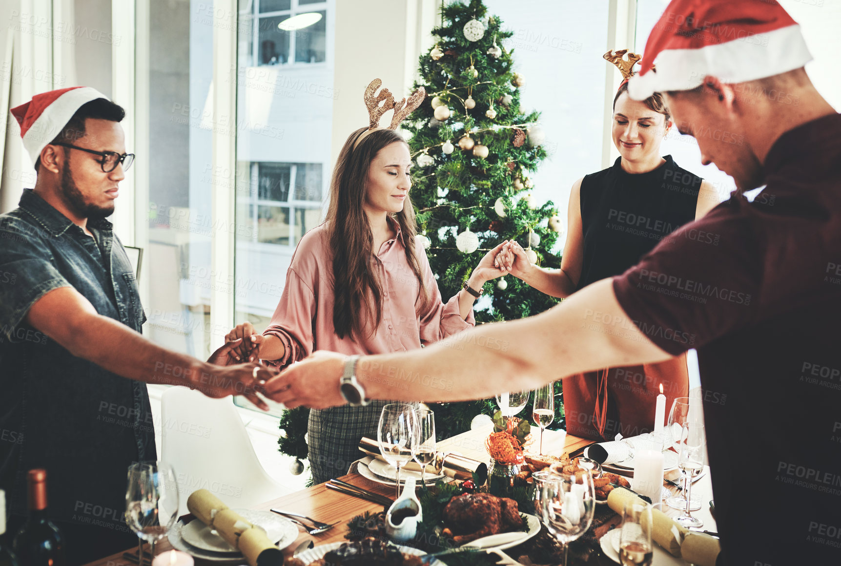 Buy stock photo Cropped shot of a group of young friends saying grace while dining together at Christmas