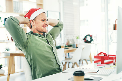 Buy stock photo Shot of a young businessman relaxing with his hands behind his head while working in his office on Christmas Eve