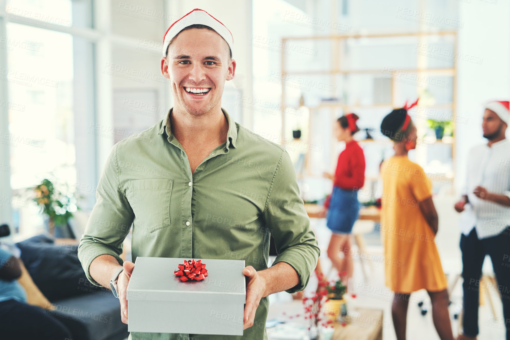 Buy stock photo Portrait of a handsome young businessman holding a gift box at an office Christmas party with colleagues in the background