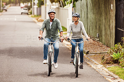 Buy stock photo Shot of a cheerful senior couple riding on bicycles together outside in a suburb