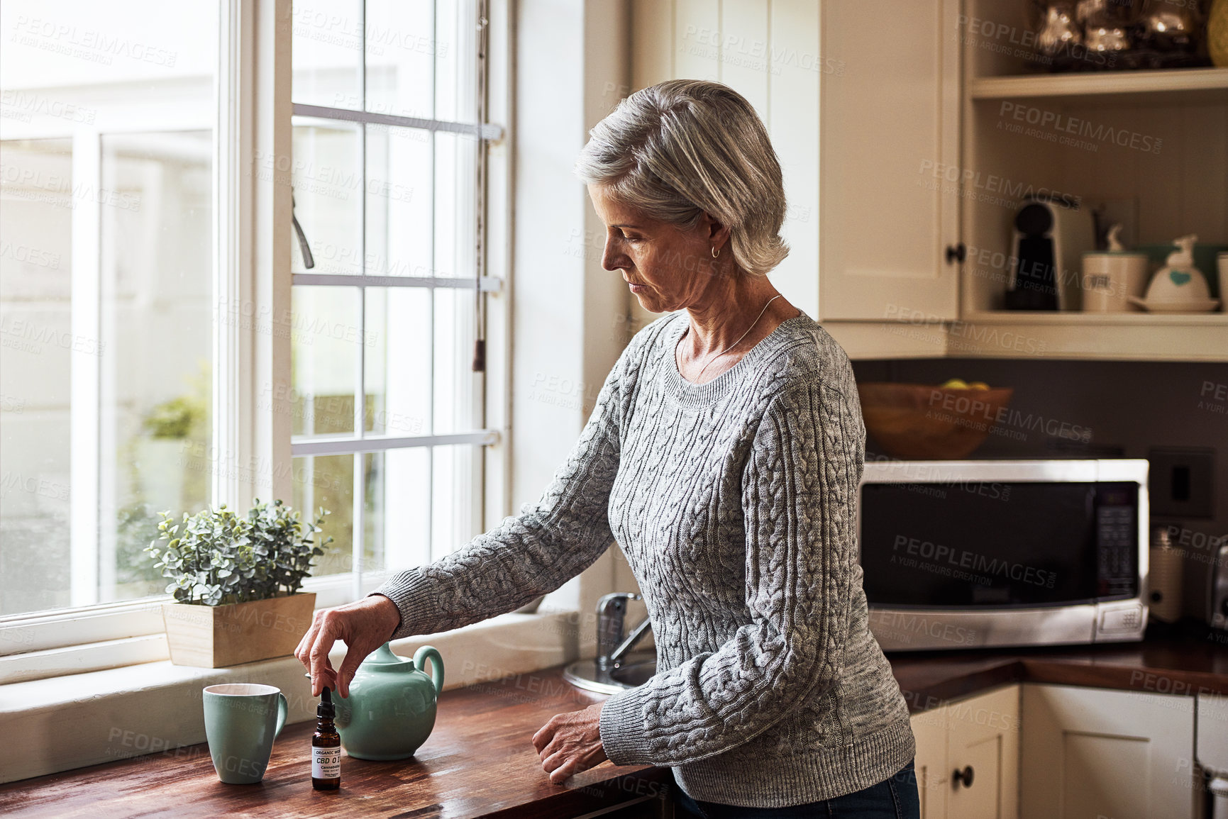 Buy stock photo Cropped shot of a relaxed senior woman preparing a cup of tea with CBD oil inside of it at home during the day