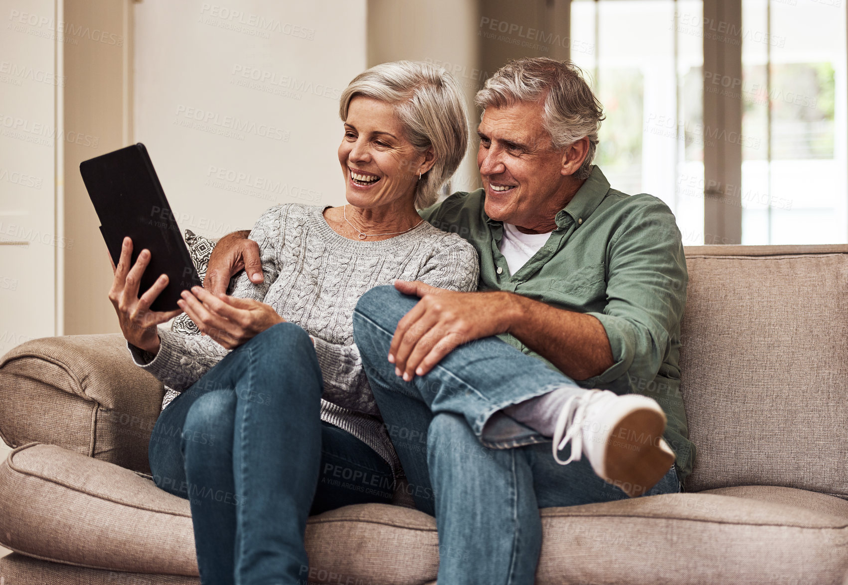 Buy stock photo Cropped shot of a cheerful senior couple browsing on a digital tablet together while being seated on a couch at home during the day