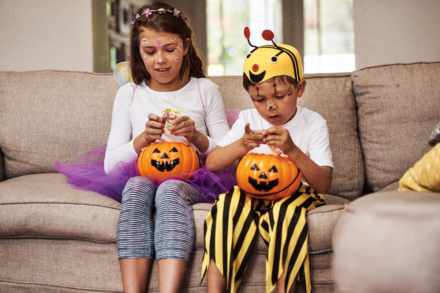 Buy stock photo Halloween, sweets and children on sofa with costume for holiday event, celebration and happiness with pumpkin. Couch, young girl and boy with orange vegetable for eating candy, smile and fairy outfit