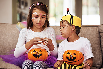 Buy stock photo Cropped shot of a young brother and sister eating their Halloween candy while sitting on their sofa at home