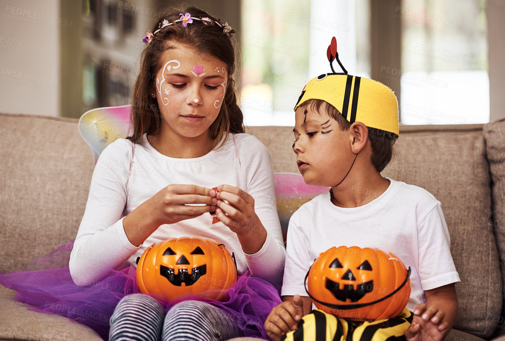 Buy stock photo Cropped shot of a young brother and sister eating their Halloween candy while sitting on their sofa at home