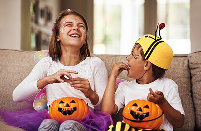 Buy stock photo Cropped shot of a young brother and sister eating their Halloween candy while sitting on their sofa at home