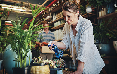 Buy stock photo Shot of an attractive young florist watering plants inside a plant nursery with her colleague also working in the background
