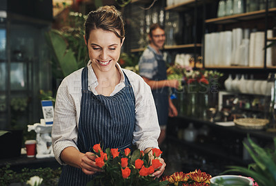 Buy stock photo Shot of an attractive young florist arranging flowers inside a plant nursery with her colleague also working in the background