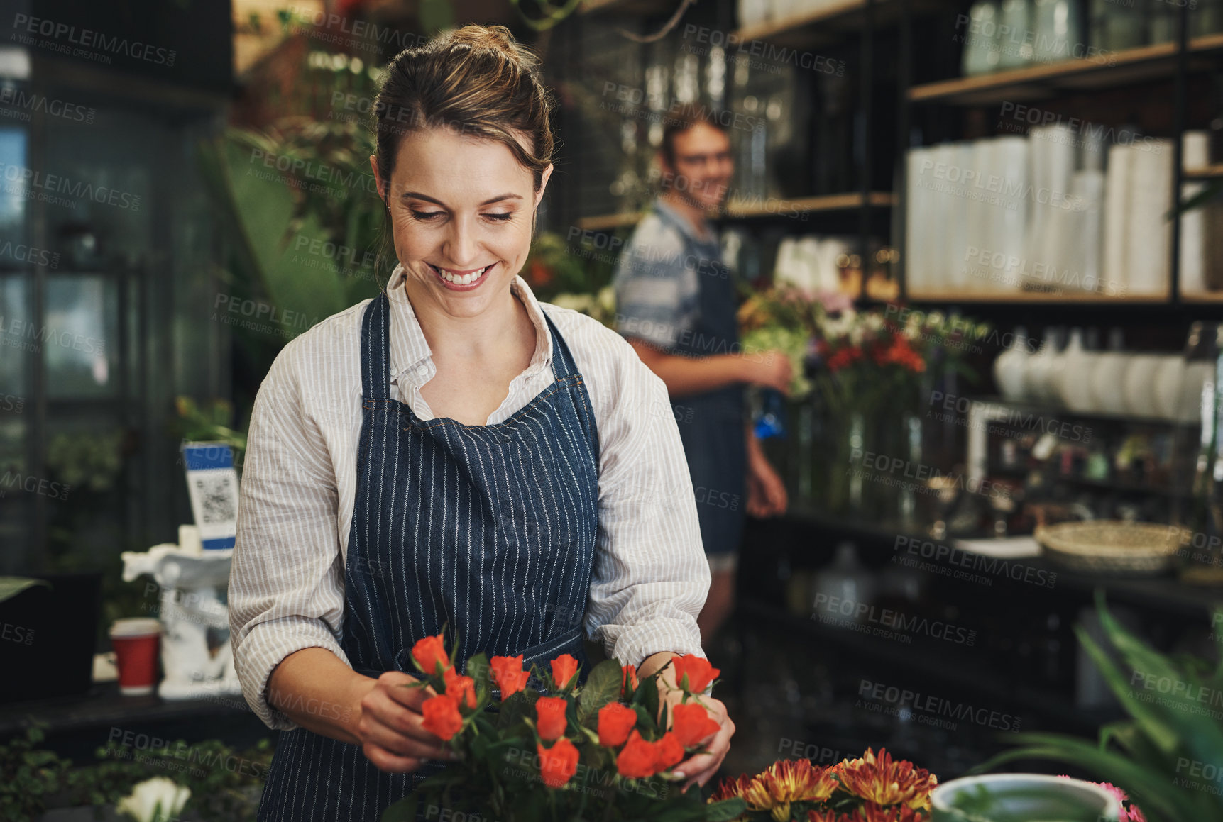 Buy stock photo Shot of an attractive young florist arranging flowers inside a plant nursery with her colleague also working in the background