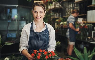 Buy stock photo Portrait of an attractive young florist arranging flowers inside a plant nursery with her colleague also working in the background