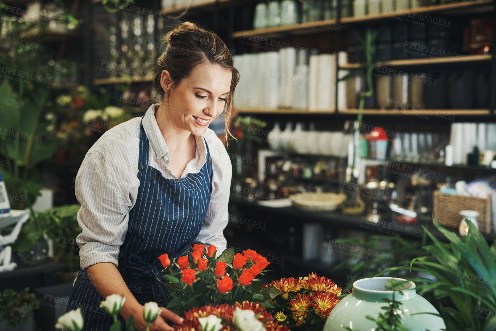 Buy stock photo Cropped shot of an attractive young florist arranging flowers inside her plant nursery