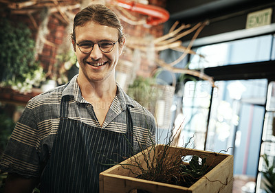 Buy stock photo Portrait of a handsome young florist holding a crate full of plants inside of his plant nursery